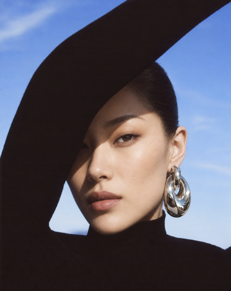 Asian woman wearing oversized shiny silver earrings in a black turtleneck